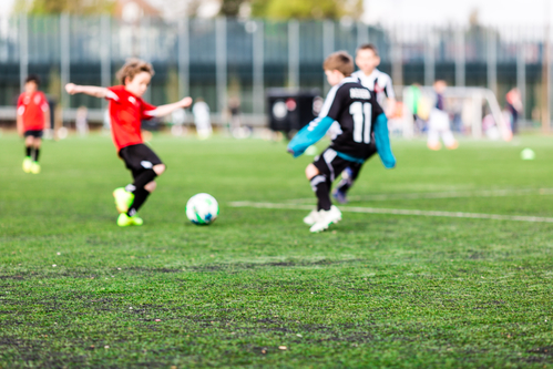 Shallow depth of field shot of young boys playing a kids soccer match on green turf.