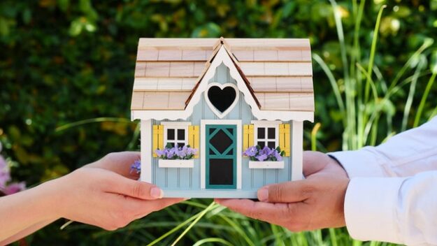 two people holding a small model of a home